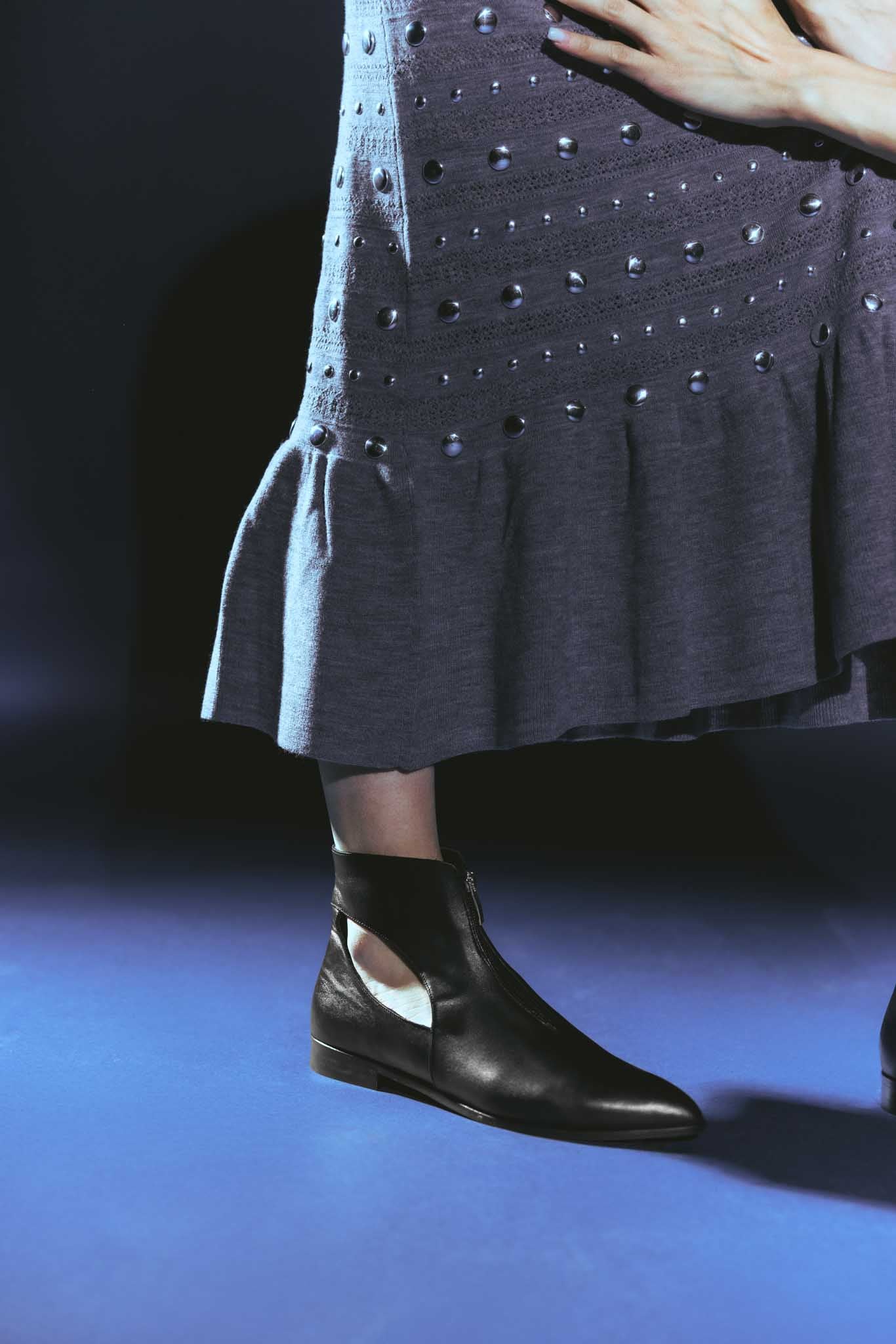 Person wearing a dark gray dress with a textured pattern and black ankle boots on a blue background